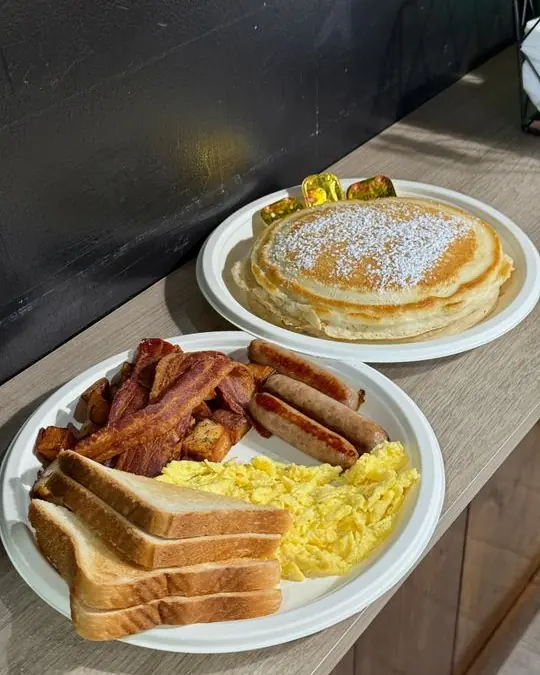 Pancakes, eggs, bacon, sausage and toast on paper plates