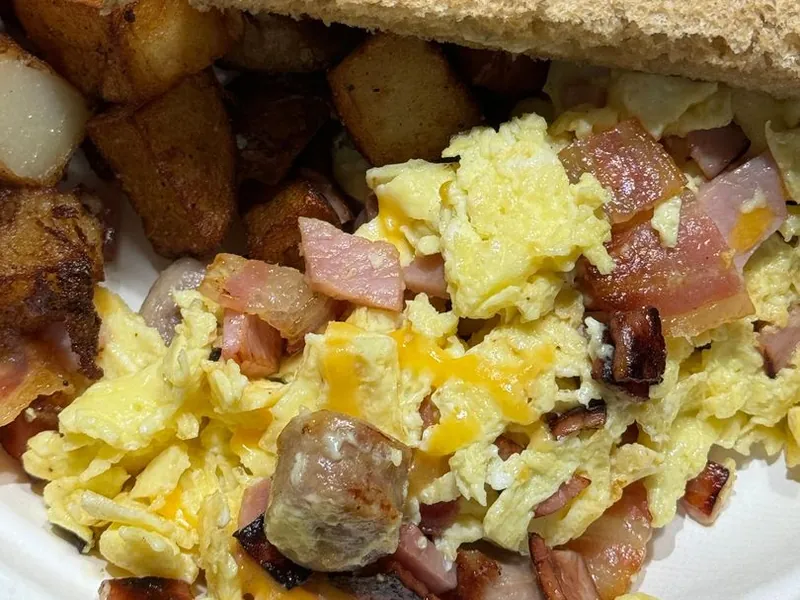 Scrambled eggs with ham, sausage and cheddar beside home fries and toast